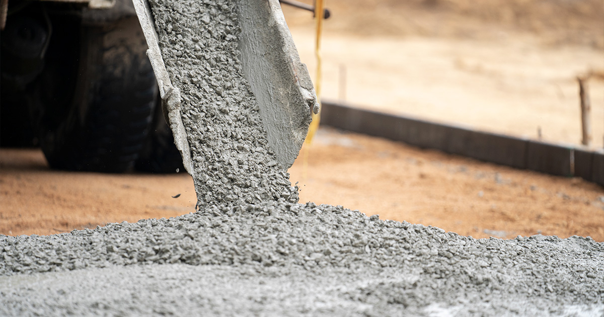 Concrete pouring off of concrete truck into frame into dirt.